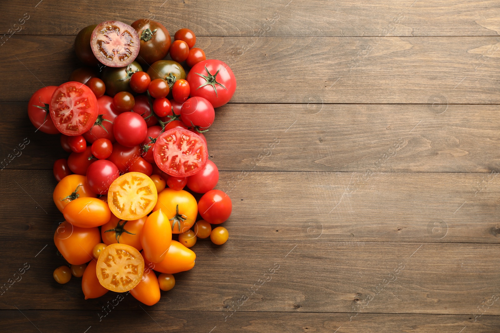 Photo of Many different ripe tomatoes on wooden table, flat lay. Space for text