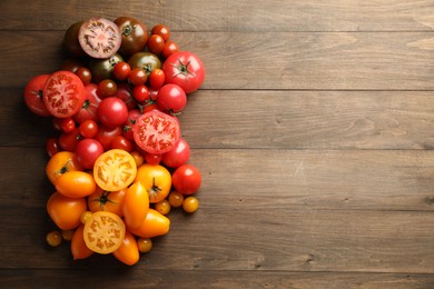 Photo of Many different ripe tomatoes on wooden table, flat lay. Space for text