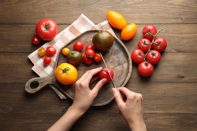 Photo of Woman cutting ripe tomatoes at wooden table, top view