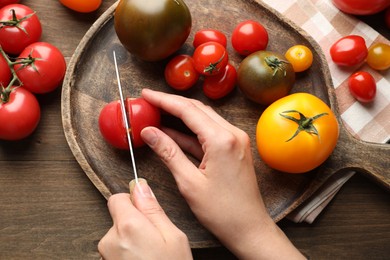 Photo of Woman cutting ripe tomatoes at wooden table, top view