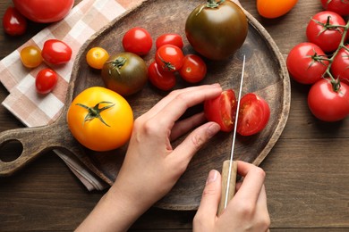 Photo of Woman cutting ripe tomatoes at wooden table, top view