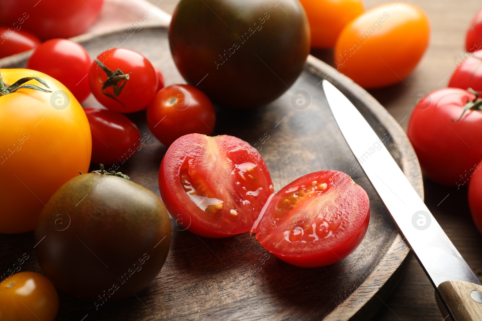 Photo of Different ripe tomatoes and knife on wooden table, closeup