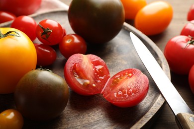 Photo of Different ripe tomatoes and knife on wooden table, closeup