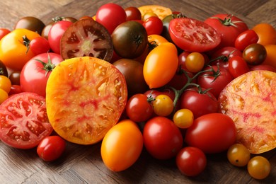 Photo of Many different ripe tomatoes on wooden table, closeup