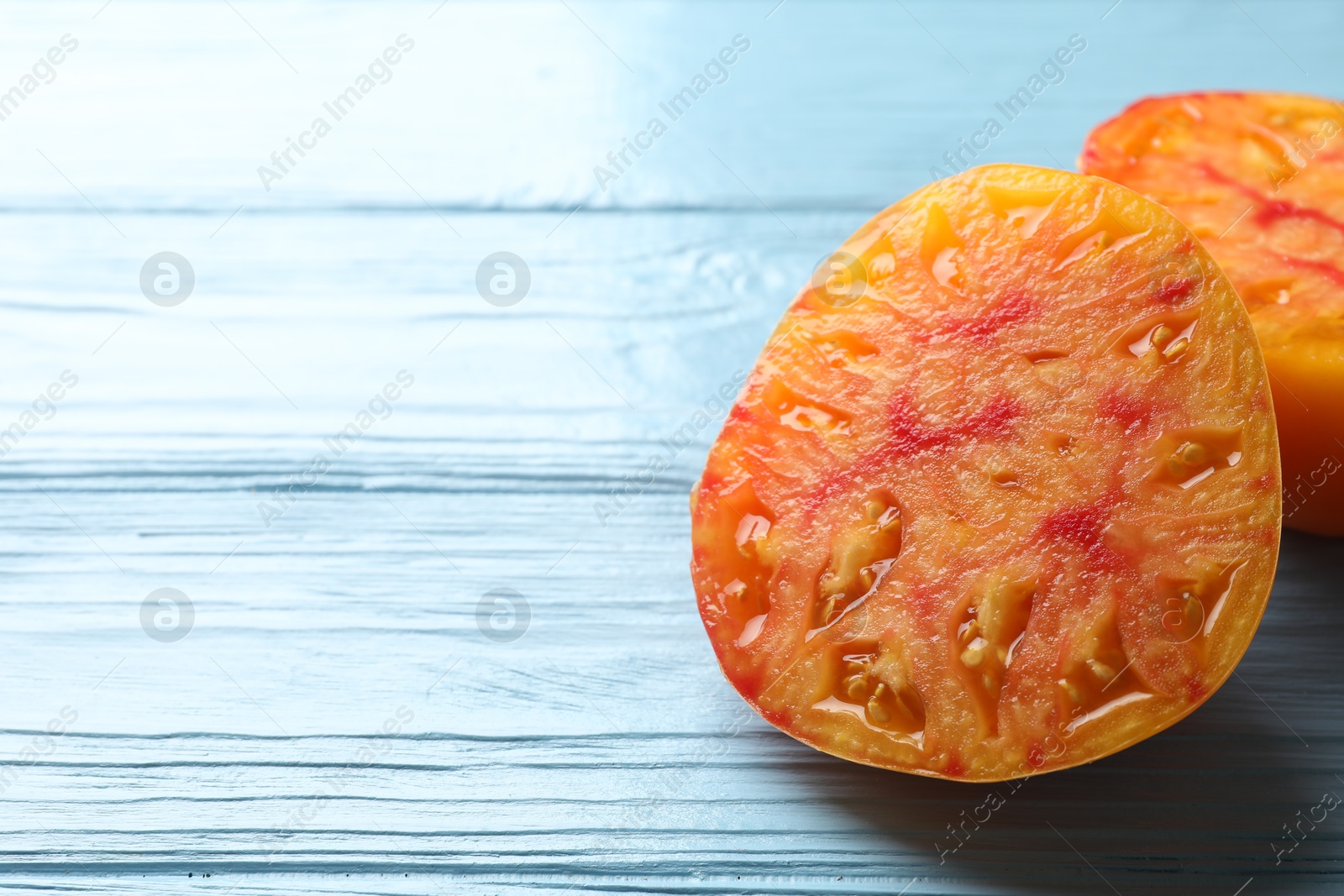 Photo of Pieces of ripe yellow tomato on light blue wooden table, closeup. Space for text
