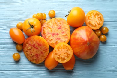 Photo of Many ripe yellow tomatoes on light blue wooden table, flat lay