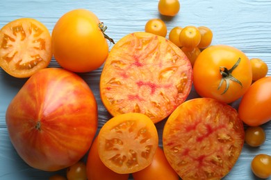 Photo of Many ripe yellow tomatoes on light blue wooden table, flat lay