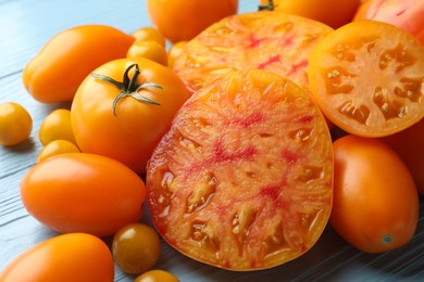 Photo of Many ripe yellow tomatoes on light blue wooden table, closeup