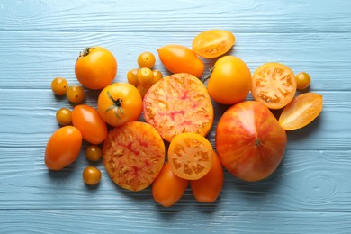Photo of Many ripe yellow tomatoes on light blue wooden table, flat lay