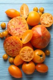 Photo of Many ripe yellow tomatoes on light blue wooden table, flat lay