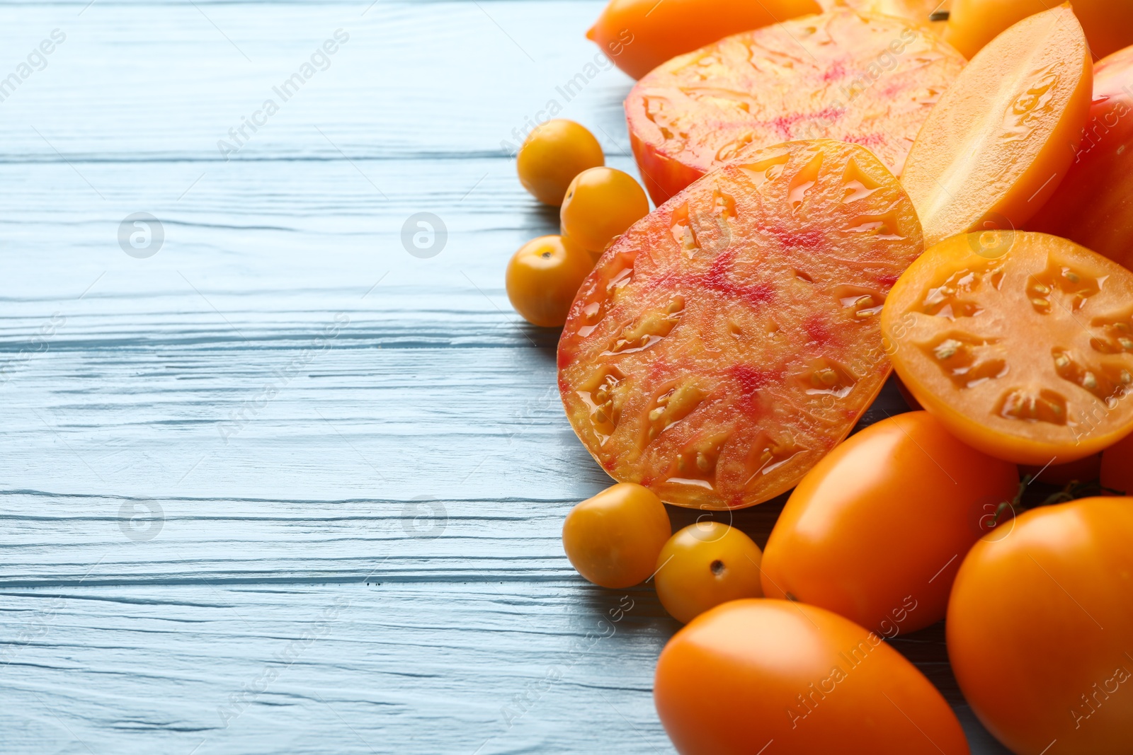 Photo of Many ripe yellow tomatoes on light blue wooden table, closeup. Space for text