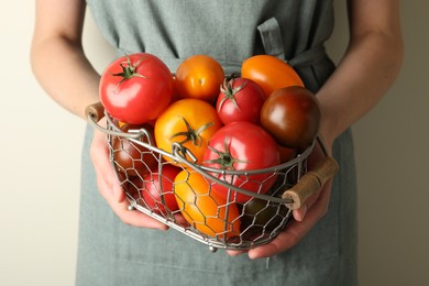 Photo of Woman with ripe tomatoes in basket on light background, closeup
