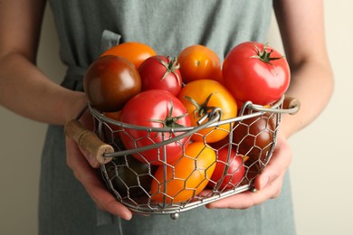 Photo of Woman with ripe tomatoes in basket on light background, closeup