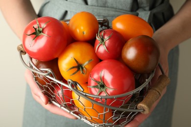 Photo of Woman with ripe tomatoes in basket on light background, closeup