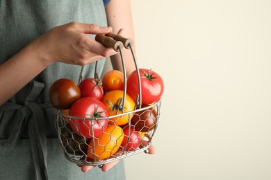Photo of Woman with ripe tomatoes in basket on light background, closeup. Space for text