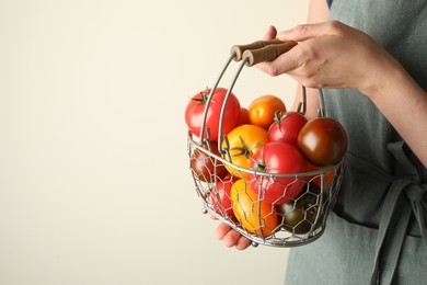 Photo of Woman with ripe tomatoes in basket on light background, closeup. Space for text