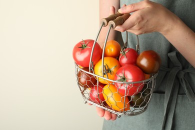 Photo of Woman with ripe tomatoes in basket on light background, closeup. Space for text