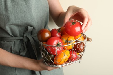 Photo of Woman with ripe tomatoes in basket on light background, closeup