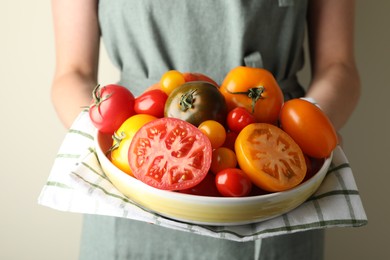 Photo of Woman with ripe tomatoes in bowl on light background, closeup