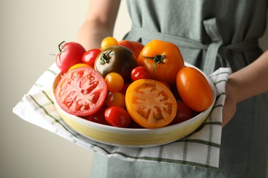Photo of Woman with ripe tomatoes in bowl on light background, closeup