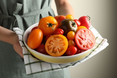 Photo of Woman with ripe tomatoes in bowl on light background, closeup