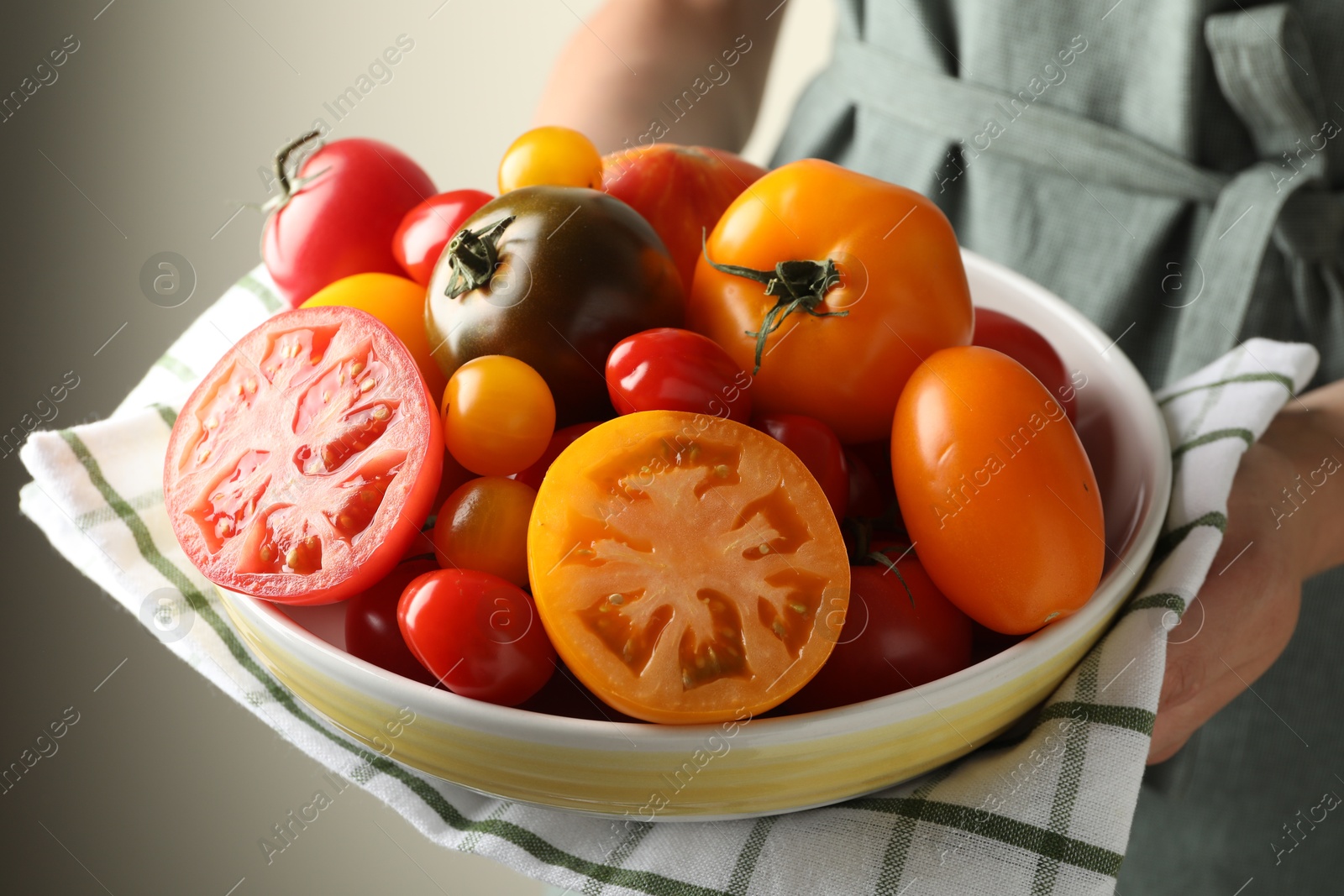 Woman with ripe tomatoes in bowl on light background, closeup Photo of Woman with ripe tomatoes in bowl on light background, closeup