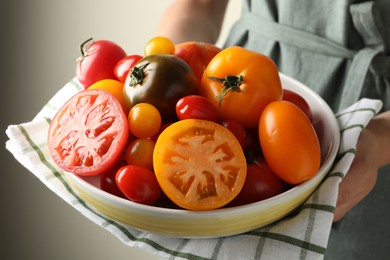 Photo of Woman with ripe tomatoes in bowl on light background, closeup