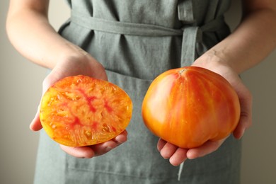 Photo of Woman with whole and cut yellow tomatoes on light background, closeup