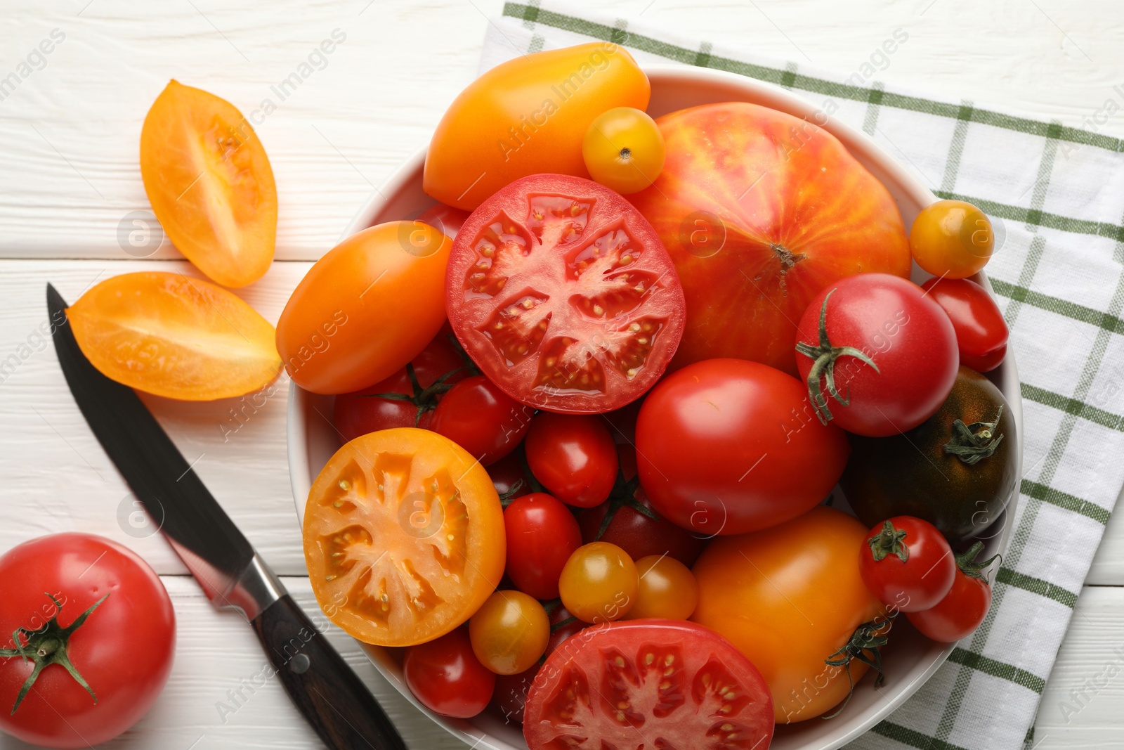Photo of Different ripe tomatoes and knife on white wooden table, flat lay