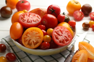 Photo of Different ripe tomatoes and knife on white wooden table, closeup