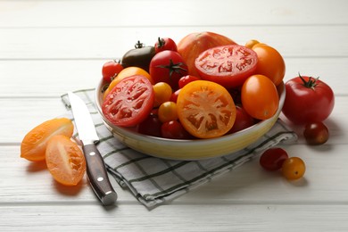 Photo of Different ripe tomatoes and knife on white wooden table, closeup