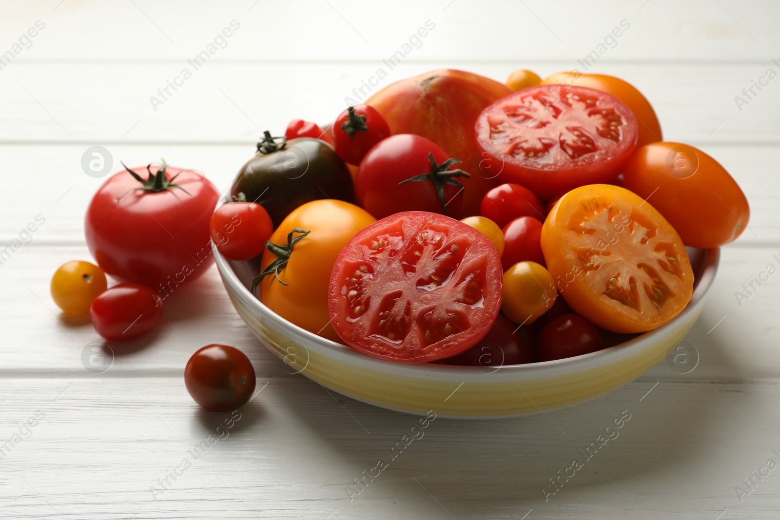 Photo of Many different ripe tomatoes on white wooden table, closeup