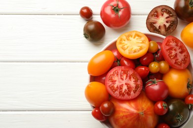 Photo of Many different ripe tomatoes on white wooden table, top view. Space for text