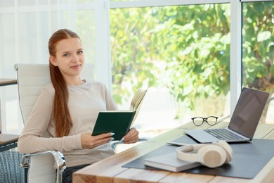 Photo of Teenage girl book and laptop at wooden desk indoors. Home workplace