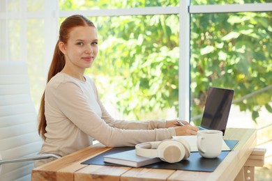 Photo of Teenage girl using laptop at wooden desk indoors. Home workplace