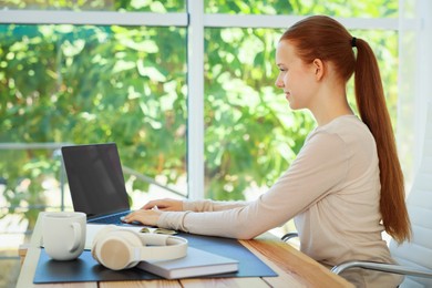 Photo of Teenage girl using laptop at wooden desk indoors. Home workplace