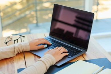 Photo of Teenage girl using laptop at wooden desk indoors, closeup. Home workplace