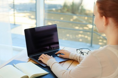 Photo of Teenage girl using laptop at wooden desk indoors, closeup. Home workplace
