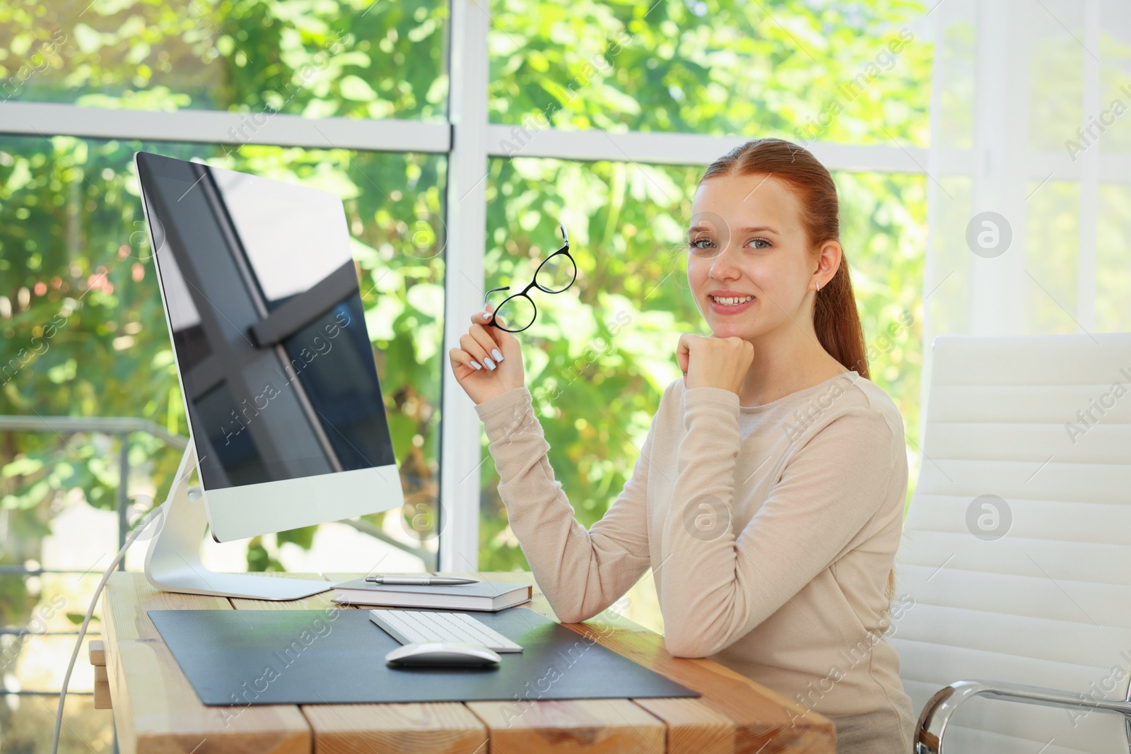 Photo of Teenage girl using computer at wooden desk indoors. Home workplace