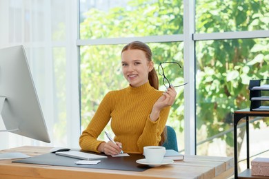 Photo of Teenage girl using computer and writing in notebook at wooden desk indoors. Home workplace