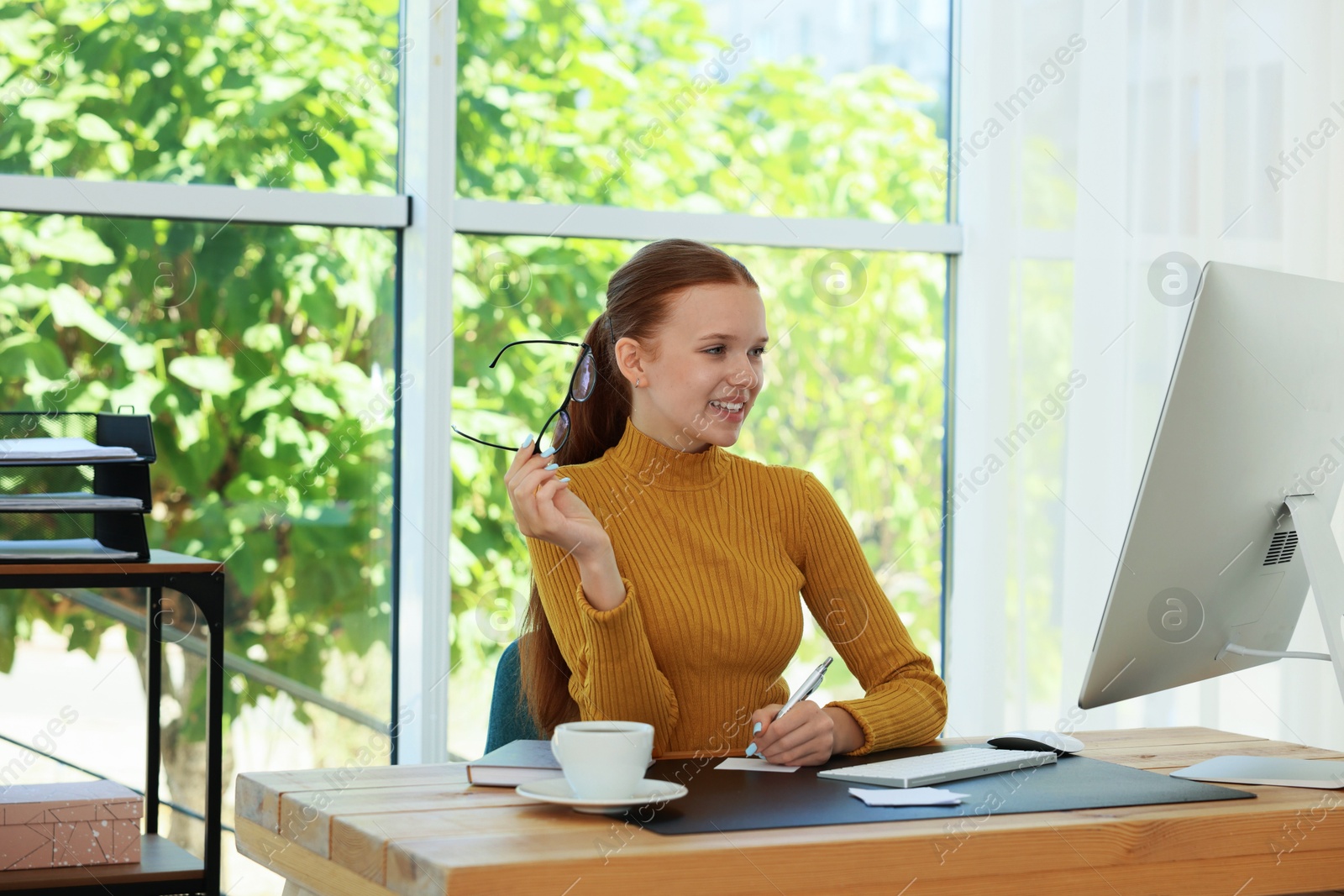 Photo of Teenage girl using computer and writing in notebook at wooden desk indoors. Home workplace