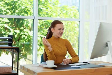 Photo of Teenage girl using computer and writing in notebook at wooden desk indoors. Home workplace