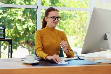 Photo of Teenage girl using computer at wooden desk indoors. Home workplace