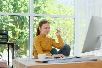 Photo of Teenage girl using computer at wooden desk indoors. Home workplace