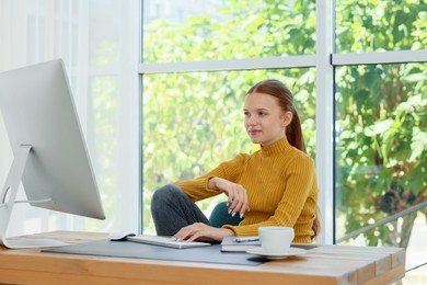 Photo of Teenage girl using computer at wooden desk indoors. Home workplace