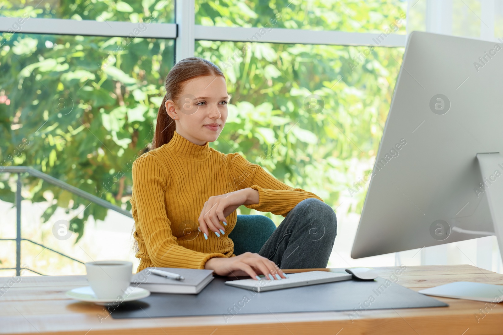 Photo of Teenage girl using computer at wooden desk indoors. Home workplace