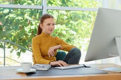 Photo of Teenage girl using computer at wooden desk indoors. Home workplace