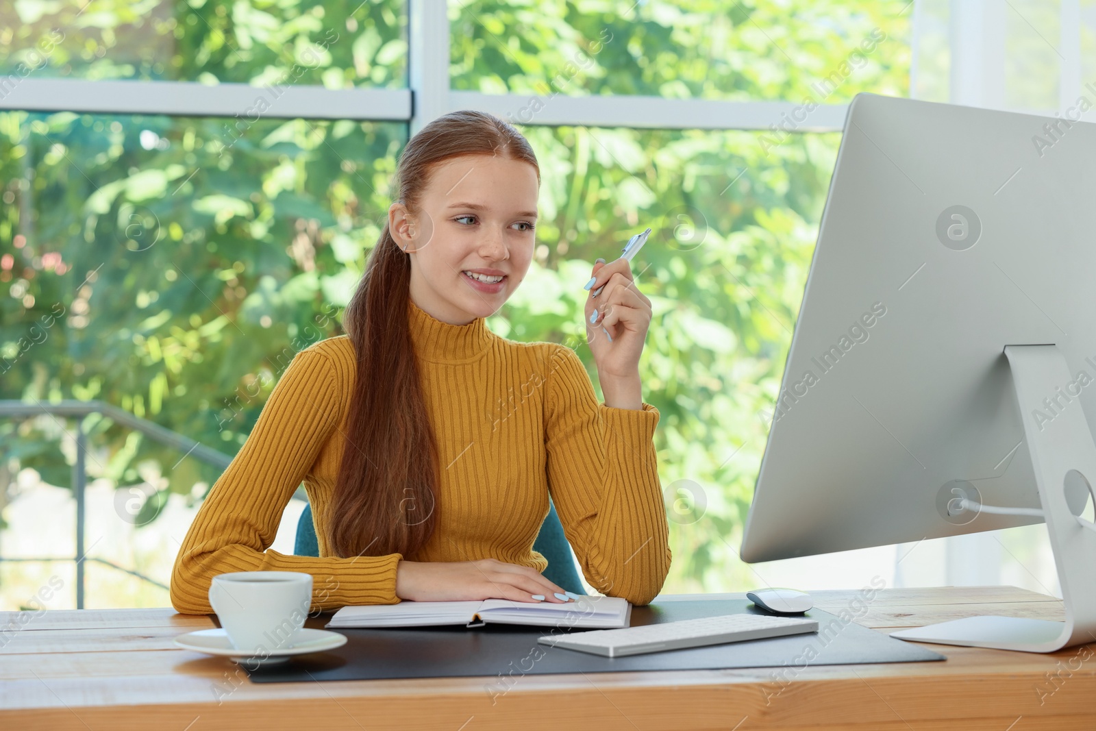 Photo of Teenage girl using computer at wooden desk indoors. Home workplace
