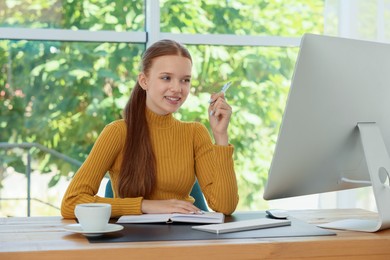 Photo of Teenage girl using computer at wooden desk indoors. Home workplace