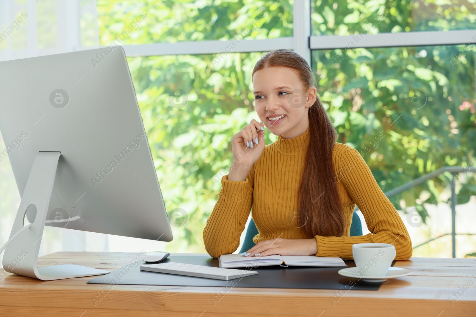 Photo of Teenage girl using computer at wooden desk indoors. Home workplace